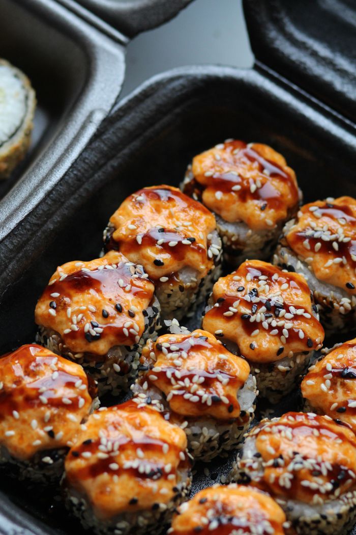 Delicious spicy sushi rolls topped with sesame seeds and sauce in a takeout container.