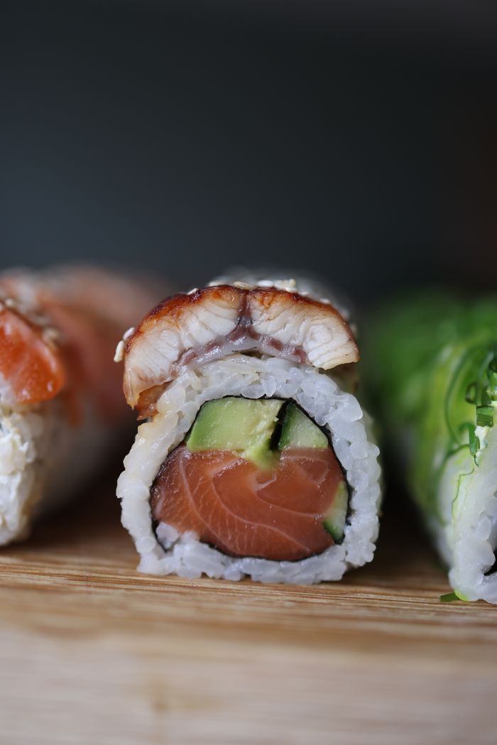 Close-up of a sushi roll with salmon, eel, avocado, and rice on a wooden board.
