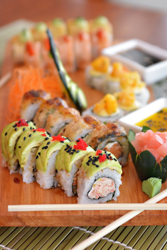 A vibrant and colorful sushi platter featuring assorted rolls topped with avocado, mango, and roe.